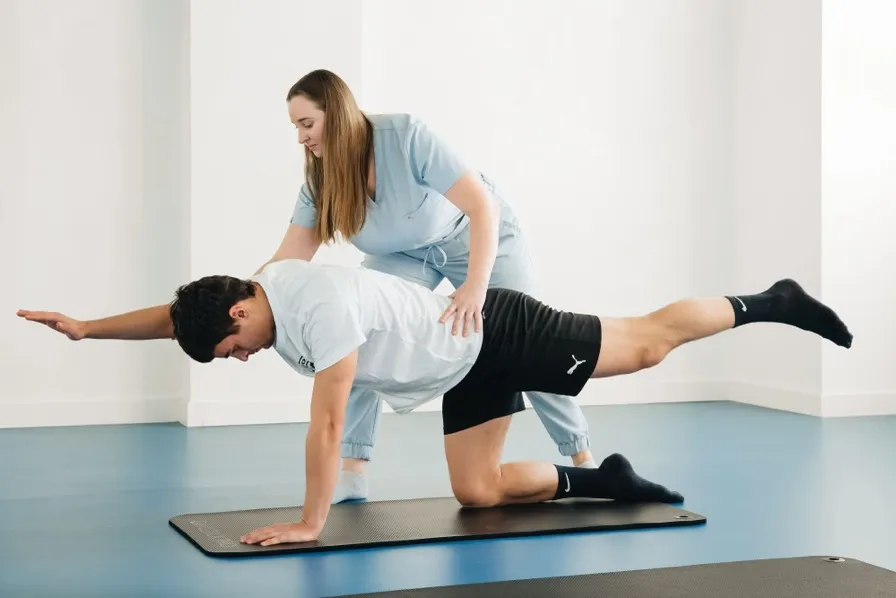 Kinésithérapeute accompagnant un patient dans un exercice de gainage sur tapis de sol, illustrant la maquette du site d’un cabinet de kinésithérapie